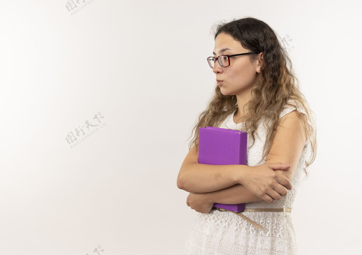 表情体贴的年轻漂亮的女学生戴着眼镜 背着书包站在侧视图里 拿着书 看着隔离在白色墙上的一面年轻包姿势