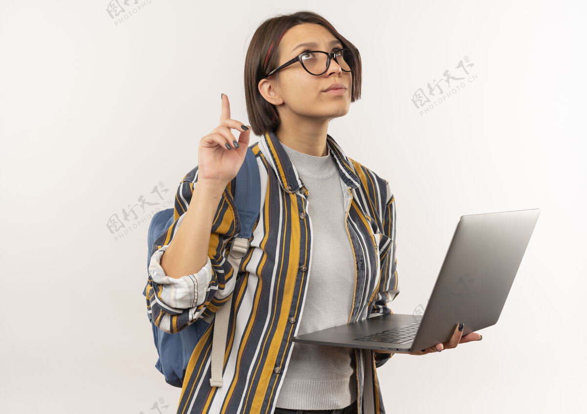 脸体贴的年轻女学生戴着眼镜 背着包拿着笔记本电脑 孤零零地指着白色的墙上背人拿着