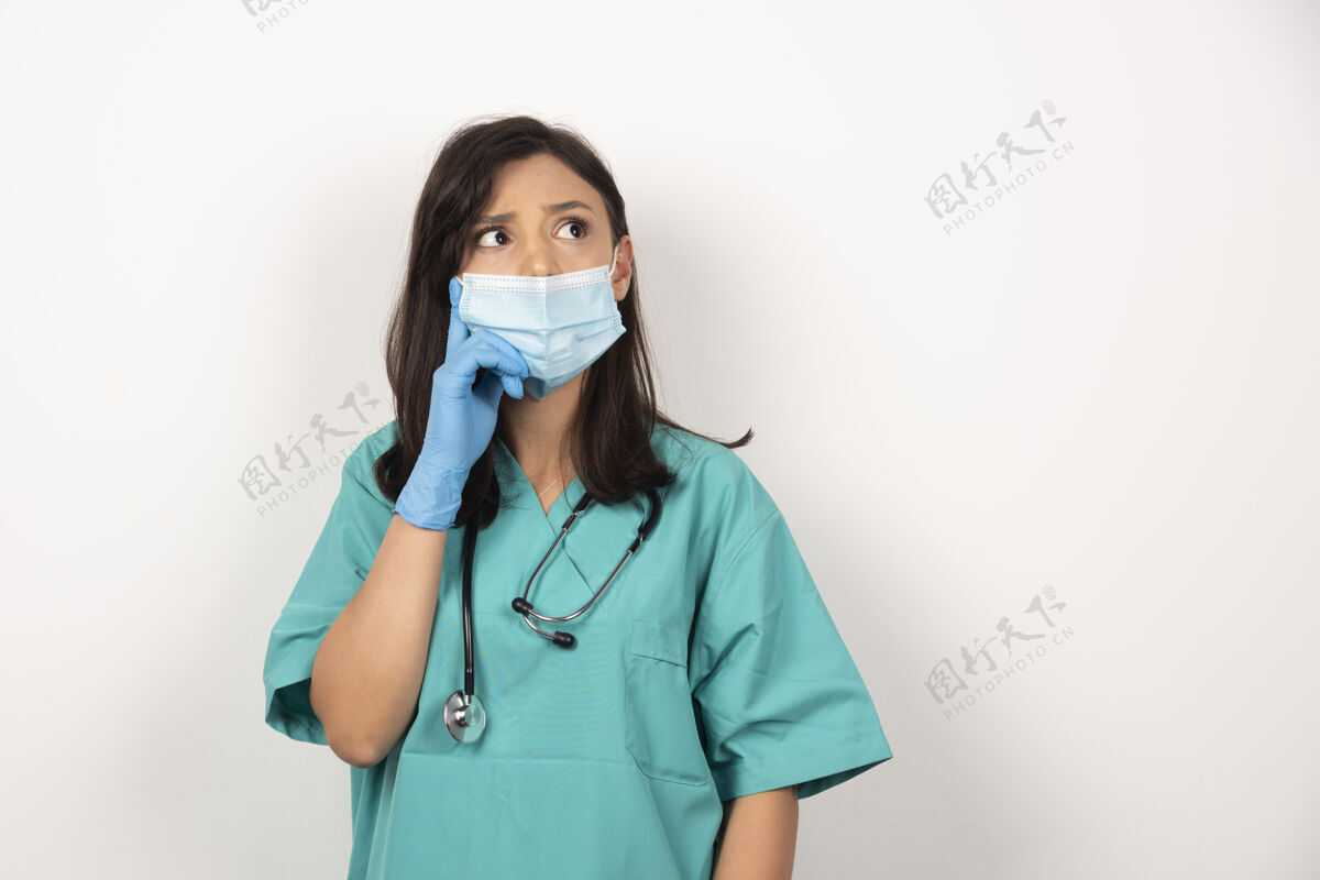 制服戴着医用面罩和手套的年轻医生在白色背景上思考高质量照片职业手套站立
