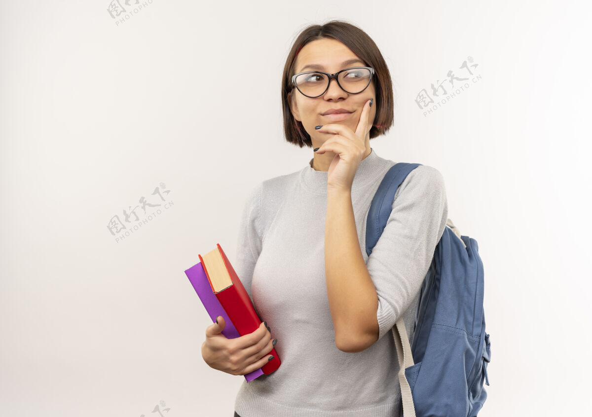 手体贴的年轻女学生戴着眼镜 背着书包 手放在下巴上 隔离在白墙上感觉年轻女孩