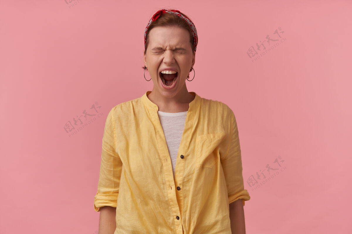 喊叫愤怒的疯女人 穿着黄色衬衫 头上戴着头巾 闭着眼睛站在粉红色的墙上尖叫凶猛尖叫压力
