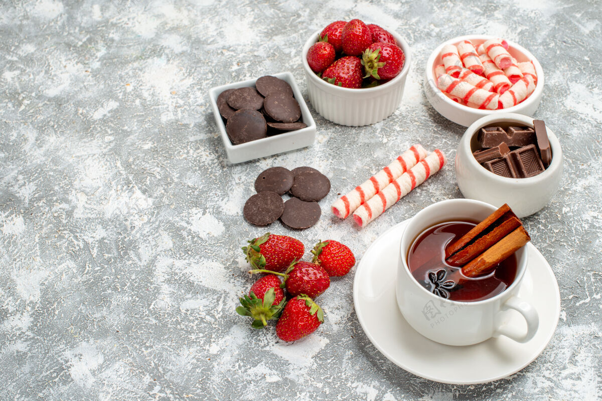 肉桂底部近距离观看碗与草莓巧克力糖果和肉桂茴香种子茶在右侧的灰白色背景食物壁板地面