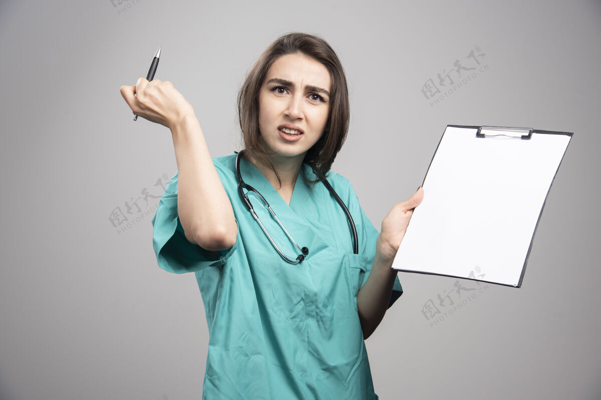 年轻人愤怒的医生拿着剪贴板在灰色背景上高质量的照片妇女制服女性