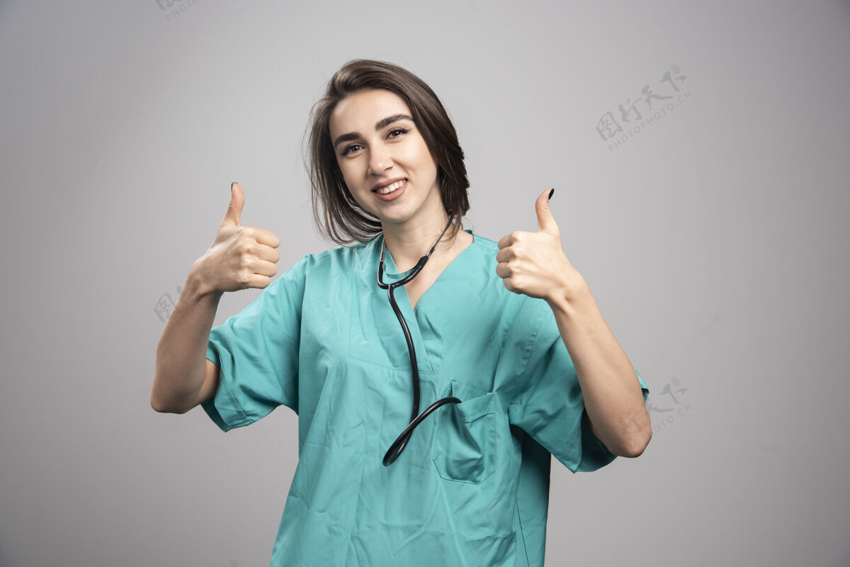 听诊器身着制服的年轻医生在灰色背景上竖起大拇指高质量照片职业个人医疗