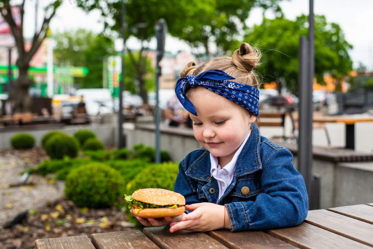 可爱在一个阳光明媚的日子里 一个迷人的微笑着的小女孩在户外拿着一个汉堡包孩子餐厅可爱