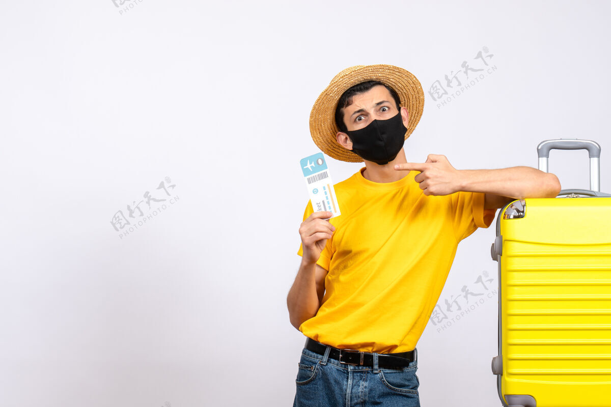 指向正面图：戴草帽的年轻人站在黄色手提箱旁 指着旅行票手提箱黄色前面
