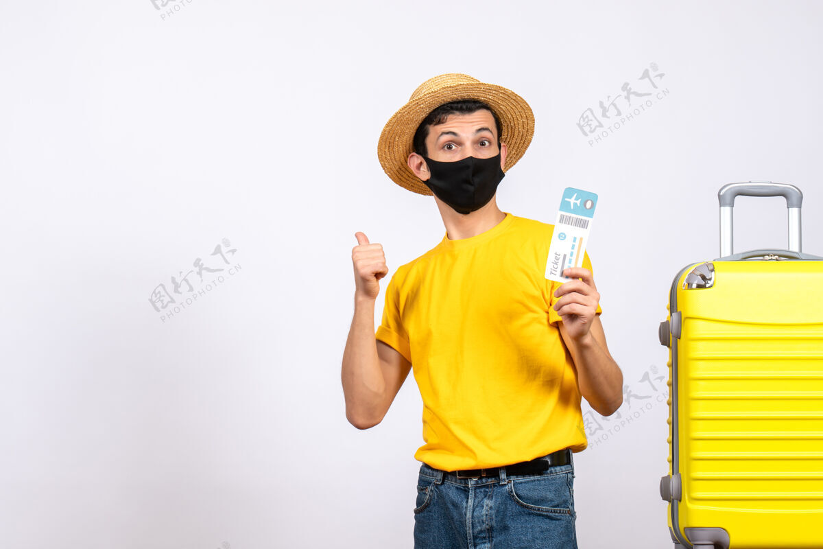 男人正面图：戴草帽的年轻人站在黄色手提箱旁 拿着旅行票 指着后面指着帽子黄色