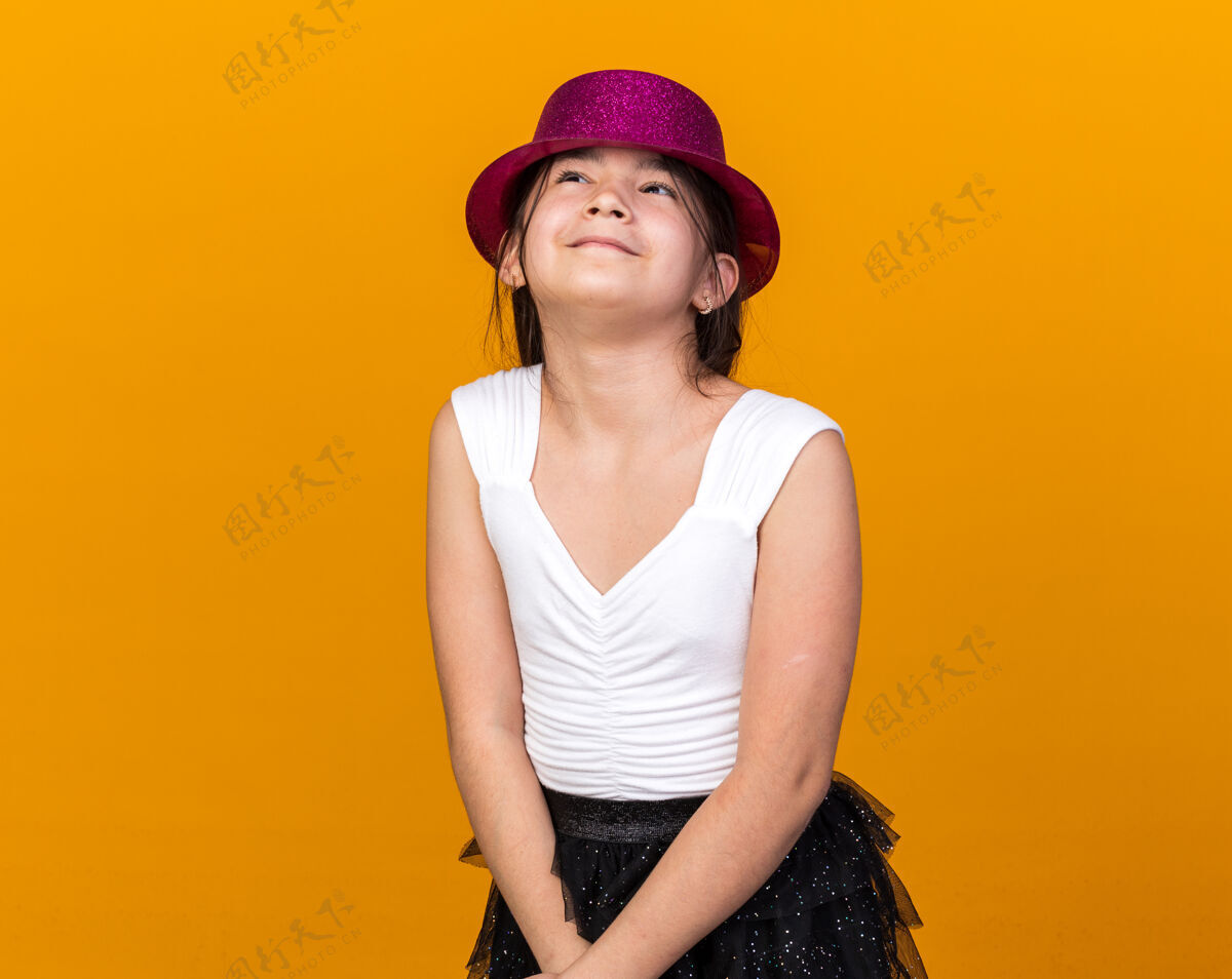 拜托戴着紫色派对帽的年轻白种女孩高兴地站在橘黄色的墙上 看着孤立的复制空间孤僻白种人女孩