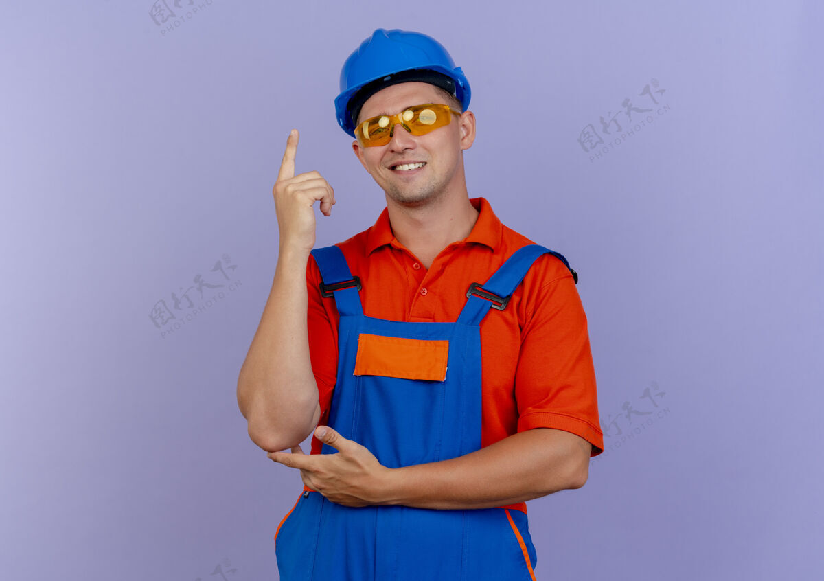 制服面带微笑的年轻男性建筑工人穿着制服 戴着安全帽和安全眼镜站在上面年轻向上紫色