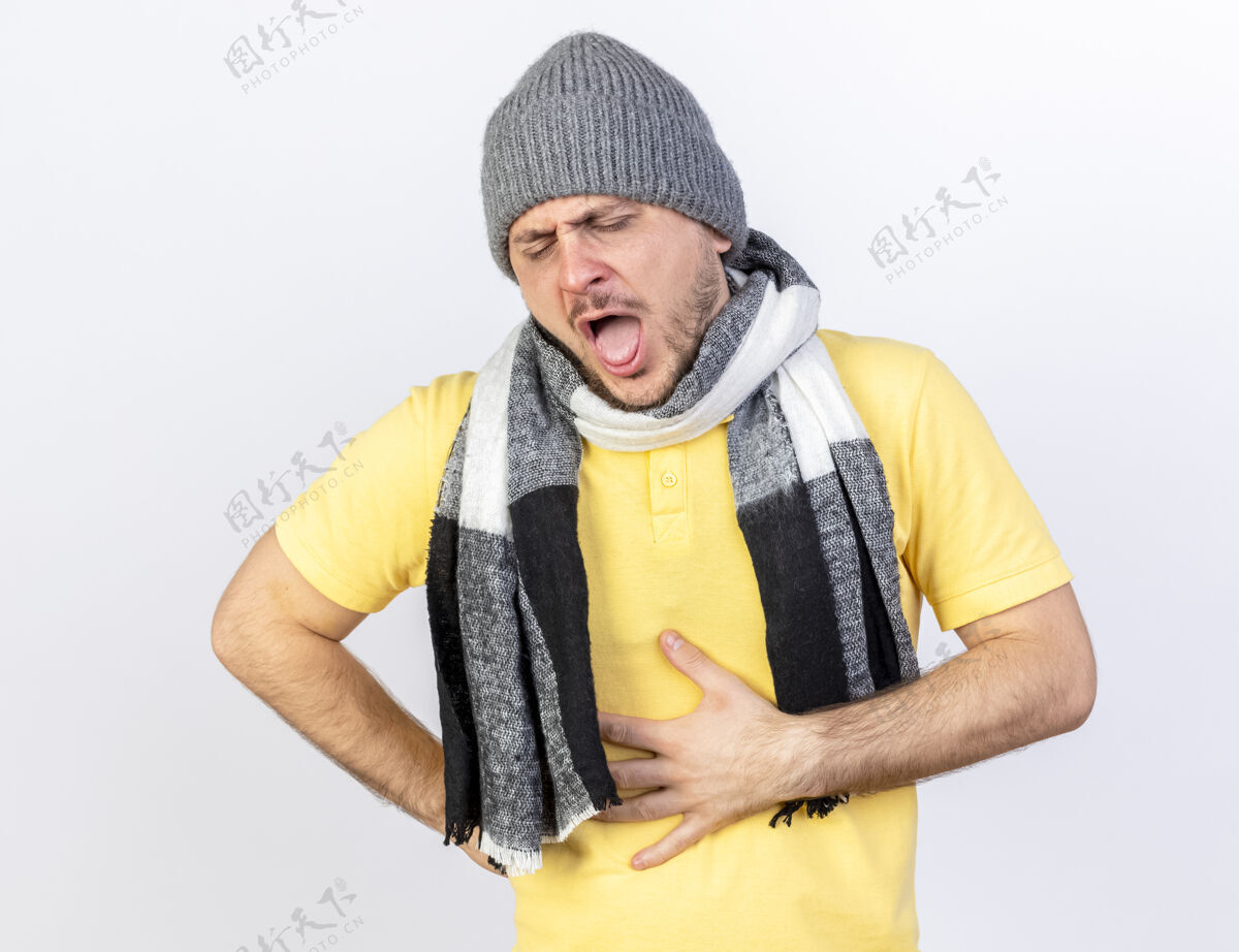 穿着年轻的金发病患戴着冬天的帽子和围巾 手放在肚子上 隔离在白墙上人脸金发