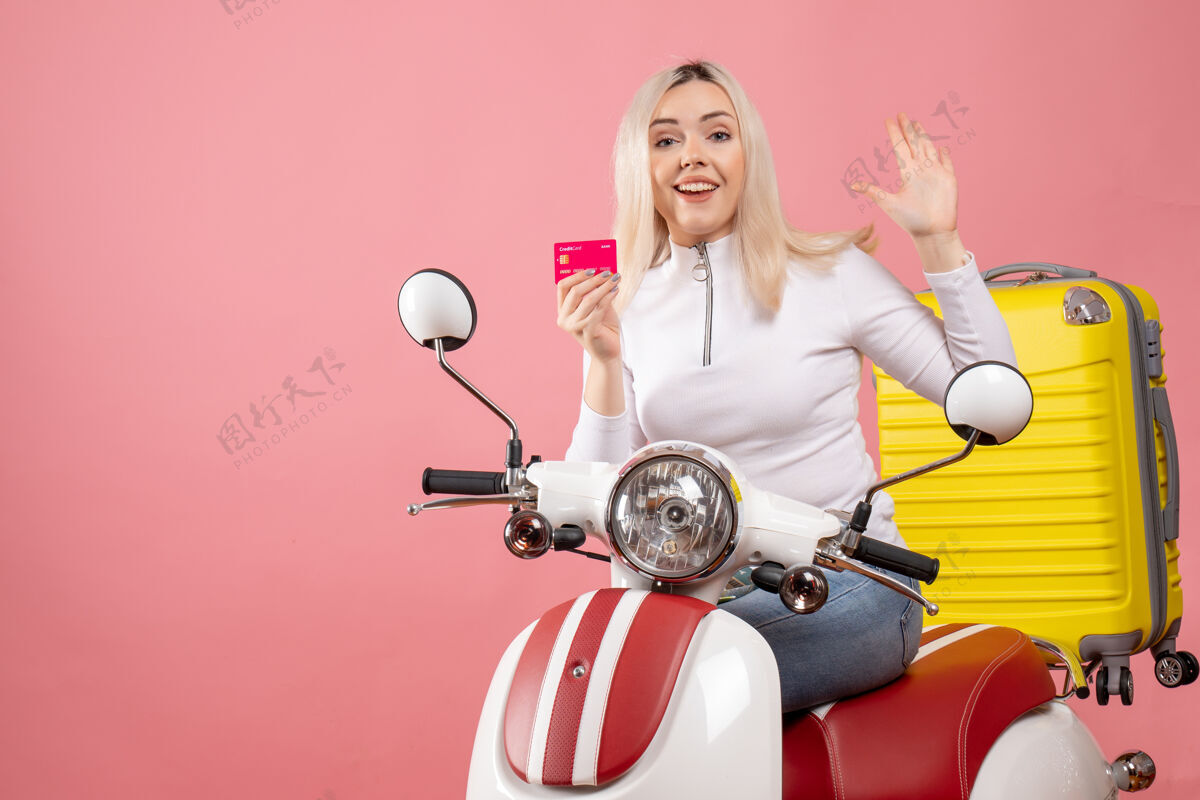 坐着前视图：骑着轻便摩托车的年轻女士 手里拿着黄色手提箱 挥舞着手轻便摩托车成人摩托车