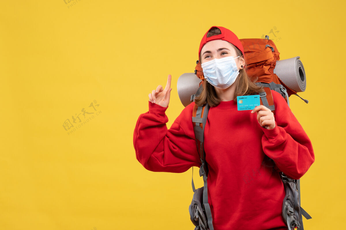 持有正面图：年轻的女性徒步旅行者 背着背包 戴着面具 拿着信用卡指着天花板安全毒气面具