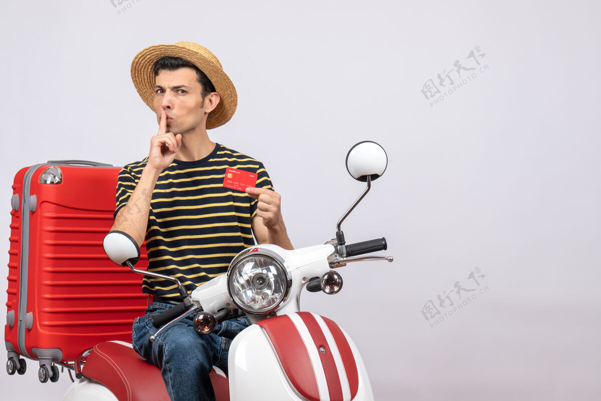 摩托车手持信用卡的手持轻便摩托车戴草帽的年轻人的正视图嘘轻便摩托车持有前面