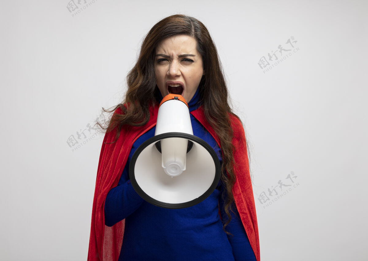 超级英雄戴着红色斗篷的恼怒女超人对着隔离在白墙上的扩音器大喊大叫恼怒大声姿势