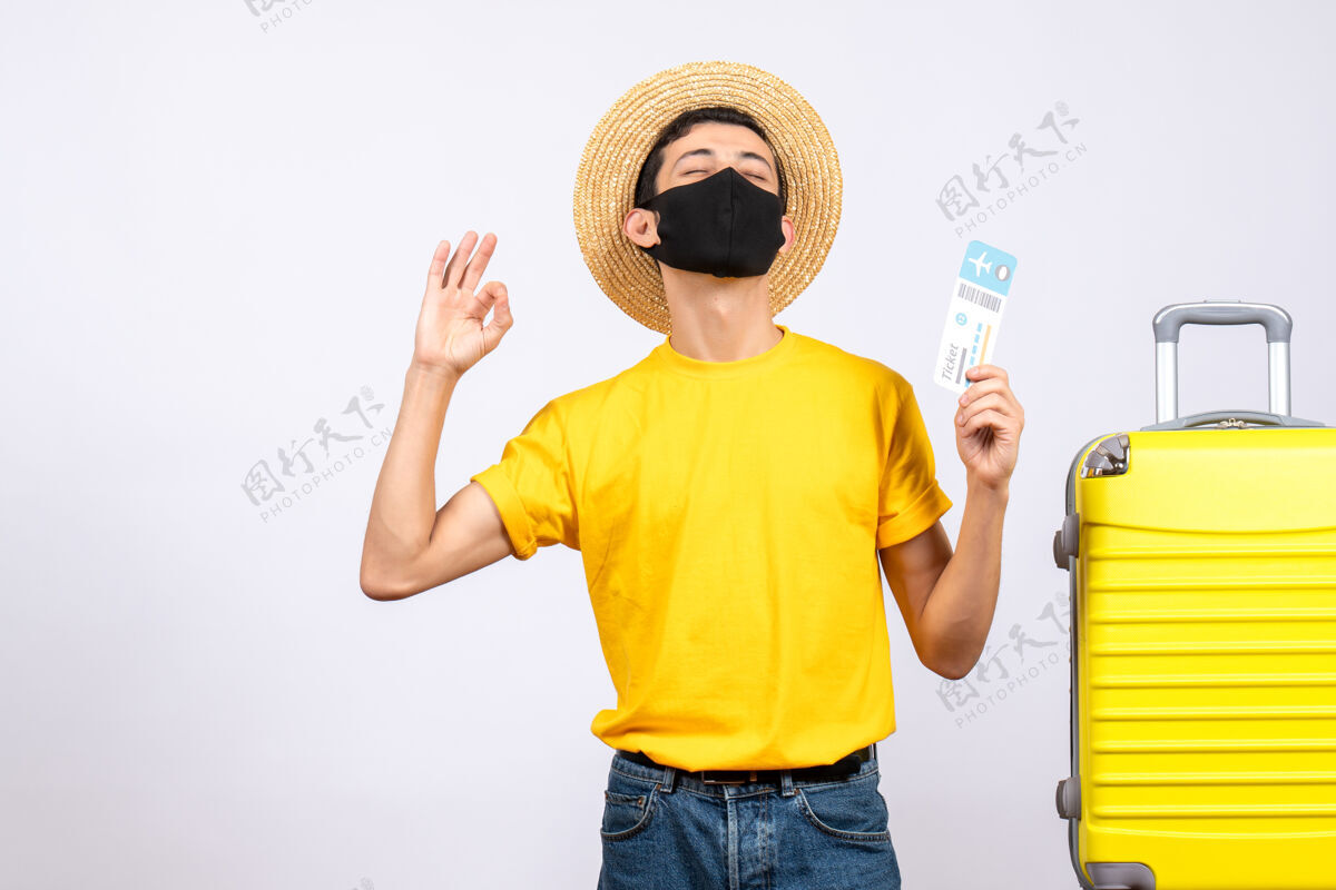 成人正面图身穿黄色t恤的年轻人站在黄色手提箱旁举着旅行票做“ok”标志向上男性黄色