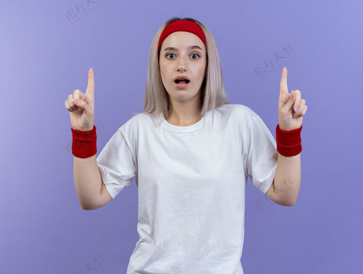 女人给人印象深刻的年轻运动女性戴着背带 戴着头带和腕带 两手孤立在紫色的墙上点手穿