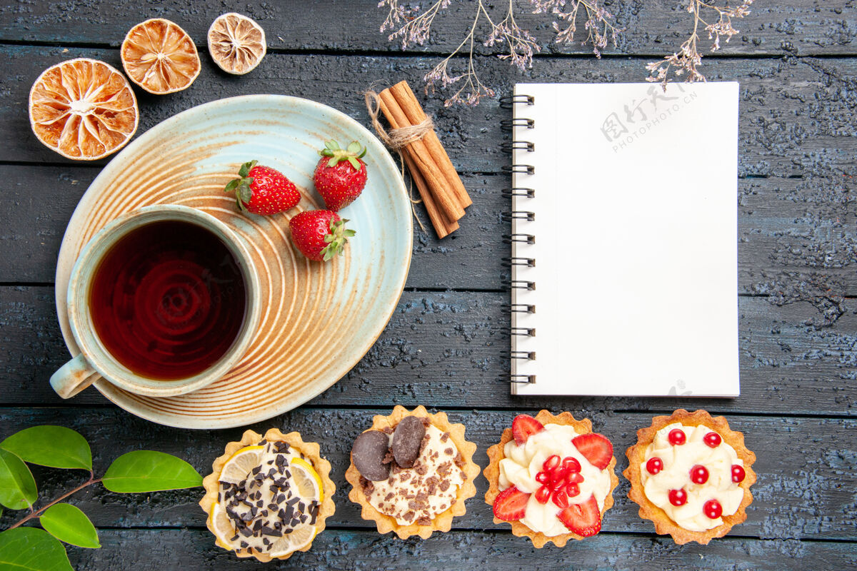 食物顶视图茶碟上的一杯茶和草莓肉桂干橙子馅饼叶子和一本深色背景的笔记本晚餐菜肴餐厅