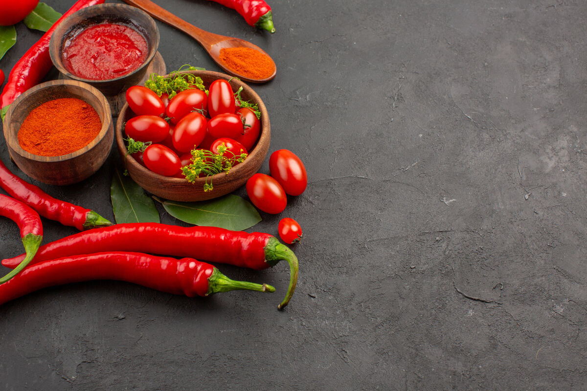 粉末俯视图一碗樱桃西红柿-红辣椒-海湾叶子-木勺-碗番茄酱和红辣椒粉-番茄在黑土地的左侧叶子海湾碗
