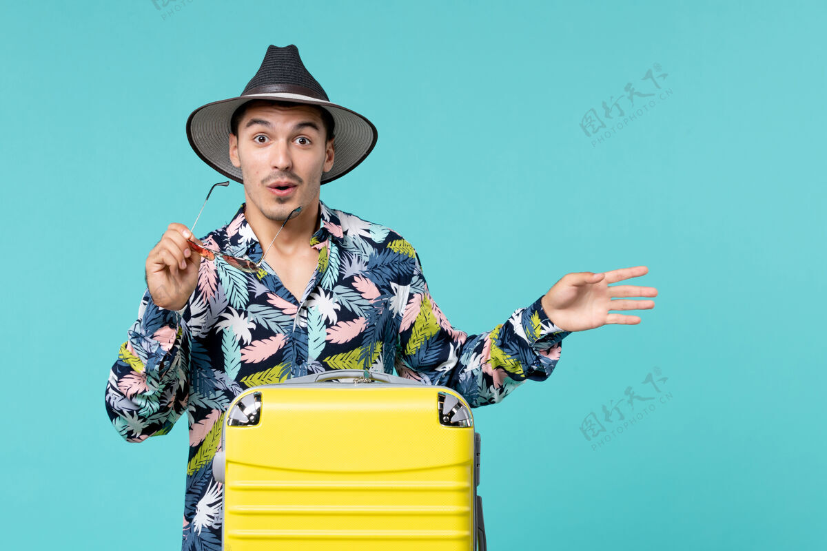 帽子年轻男子正拿着他的黄色袋子准备旅行 指着蓝色的墙上旅行旅行假期