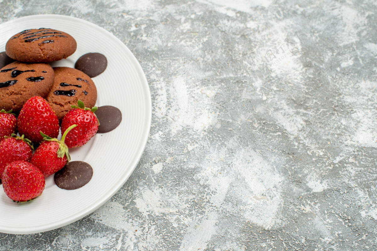 水果上半部分查看巧克力饼干草莓和圆形巧克力在白色椭圆形盘子在左侧的灰白色地面食品磨碎浆果