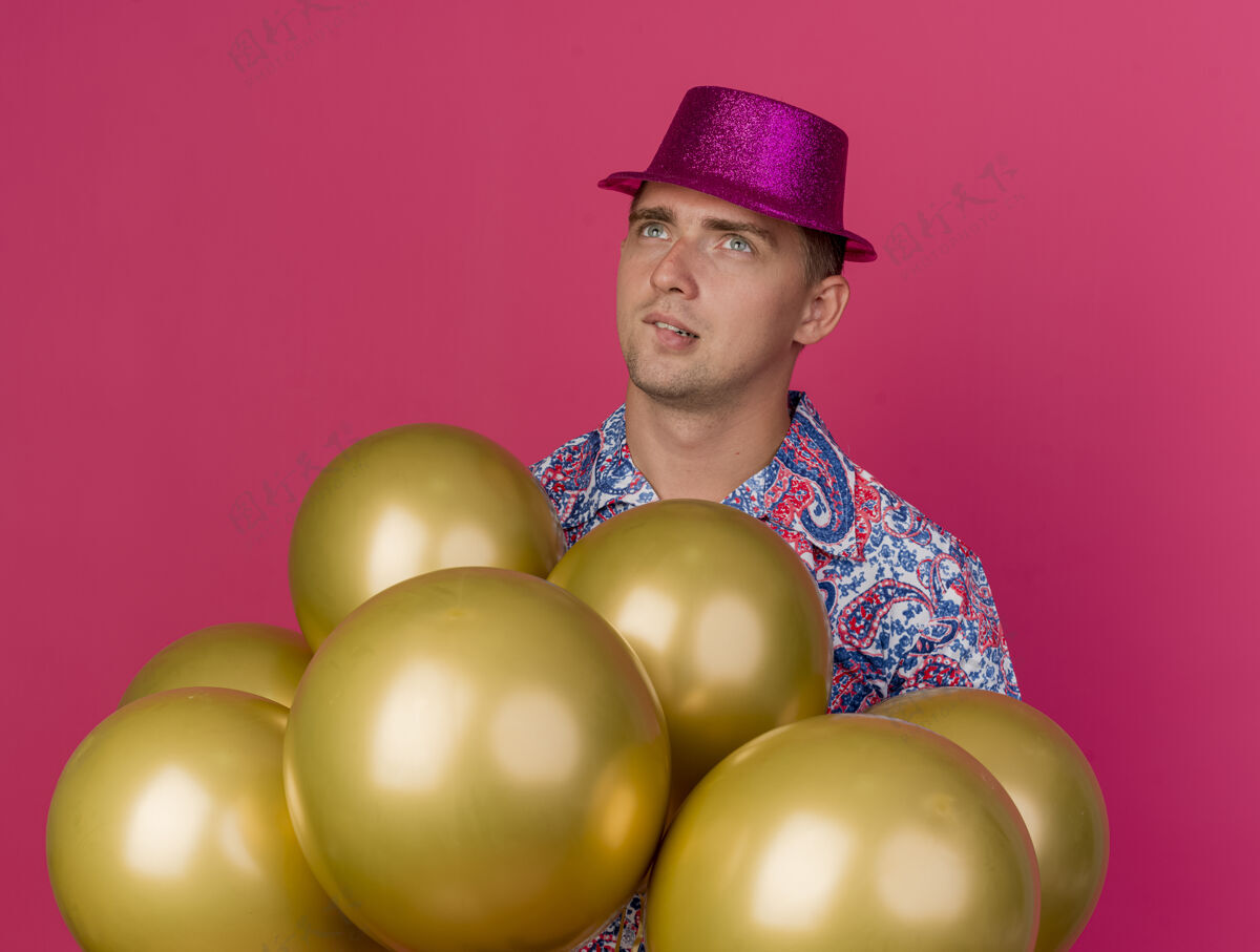 气球一个体贴的年轻人戴着粉红色的帽子站在粉红色的气球后面站着派对小伙子