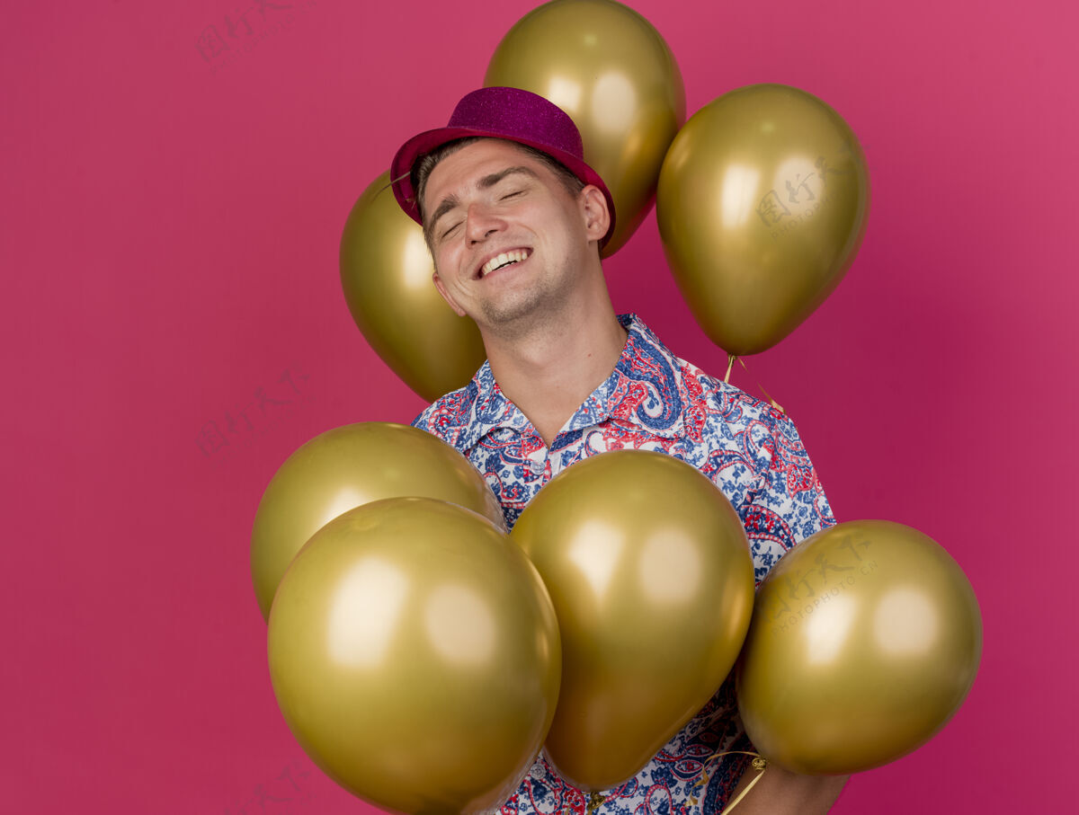 气球微笑着闭着眼睛戴着粉红色帽子的年轻人站在粉红色的气球中间年轻粉色帽子
