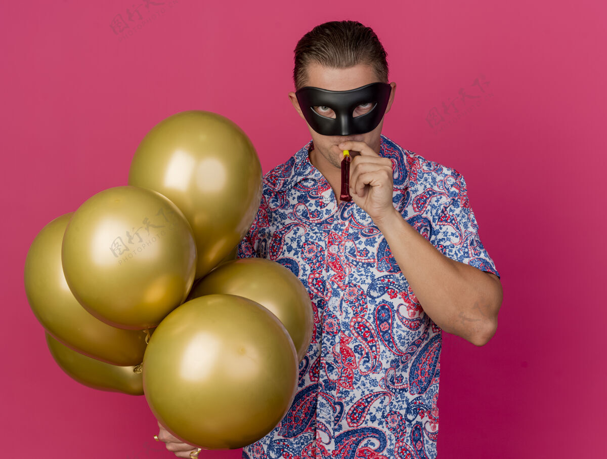 化装舞会戴着化装眼罩的年轻人拿着气球吹着粉红色的派对吹风机派对家伙举行