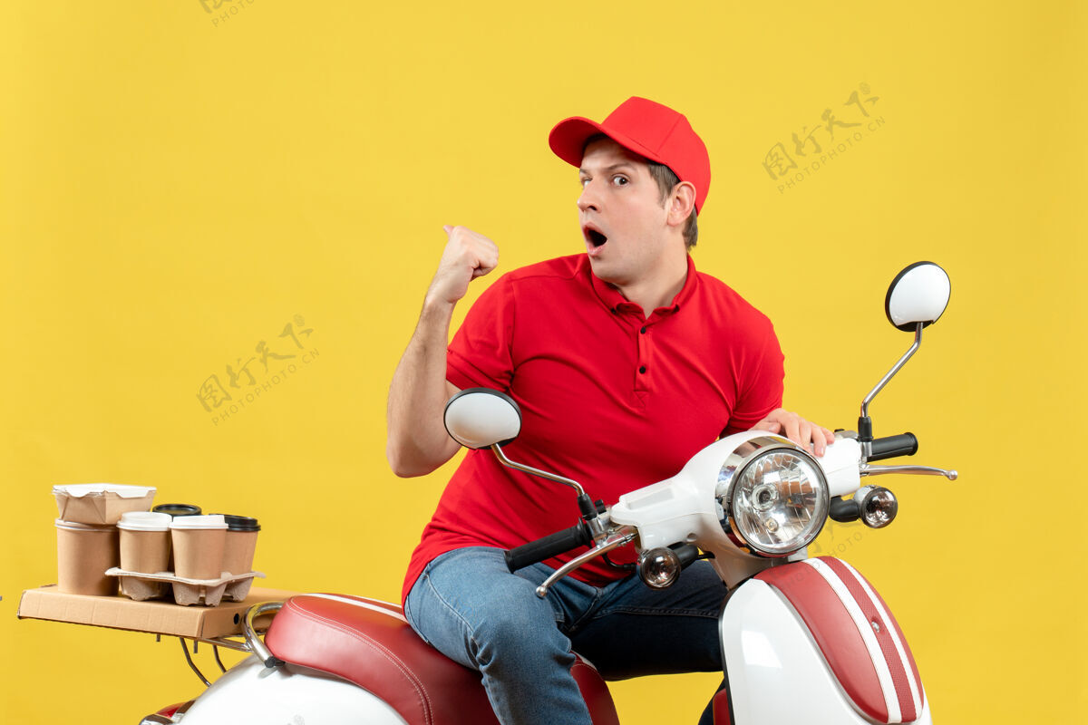交付顶视图震惊的年轻人穿着红色上衣和帽子传递命令指向黄色背景背面摩托车摩托车车辆
