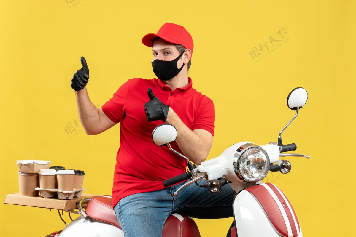 摩托车俯视图：年轻人穿着红色上衣 戴着帽子 戴着手套 戴着医用口罩 传达命令 坐在滑板车上 自信地在黄色背景上做着ok手势手套医学Ok