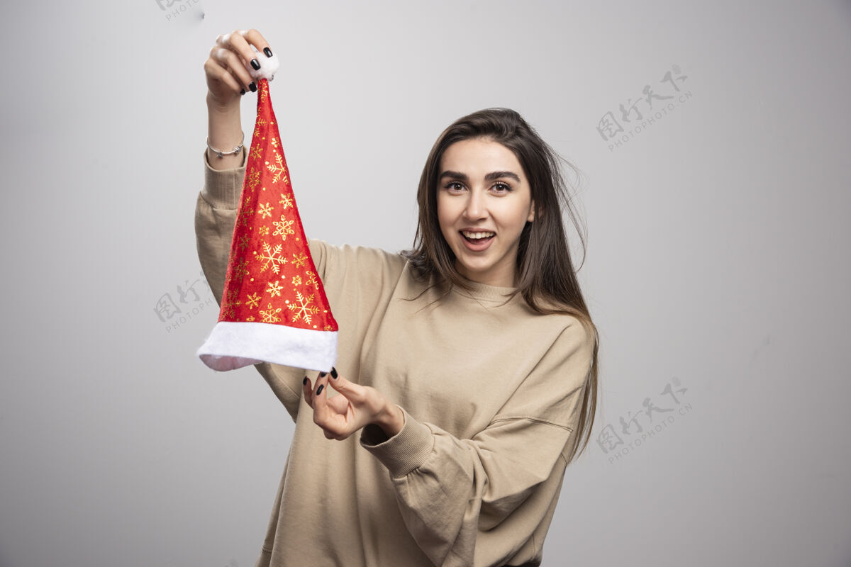 红色在灰色背景下 一个微笑的女人出现在圣诞老人的帽子前魅力模特表情