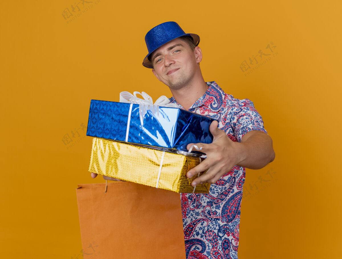橙色高兴的年轻人戴着蓝色的帽子 拿着礼品盒和橙色的袋子隔离戴着派对小伙子