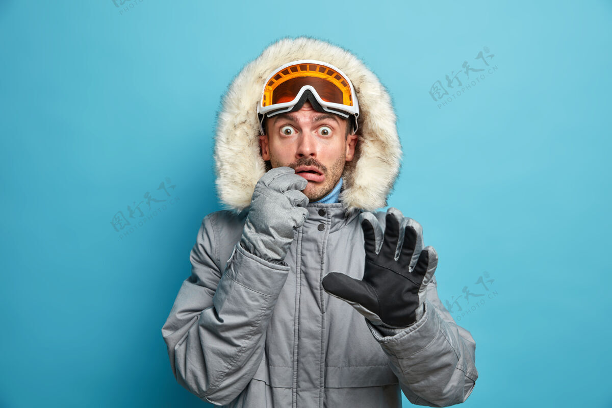 活动害怕情绪化的男滑雪者穿着暖和的夹克 戴着滑雪镜和手套 目不转睛地盯着已经活跃的寒假在山上度假年轻人害怕