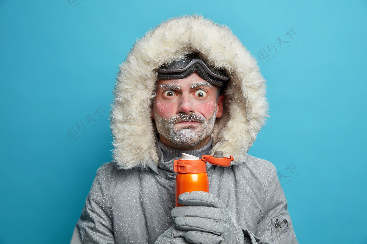 冷迷惑不解的冬衣冻人试图用热饮料取暖脸通红 熊身上覆盖着暴风雪在户外滑雪时花了很多时间寒冷的天气条件热水瓶降雪男性