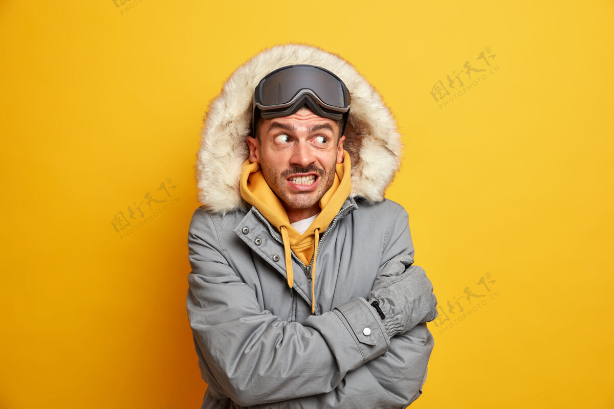 温暖帅哥觉得外面很冷 寒天里浑身发抖 抱着自己暖咬牙 穿着带兜帽的冬衣夹克季节滑雪