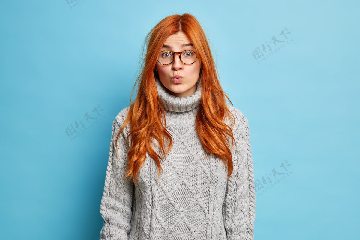 表情面部表情概念漂亮的红发欧洲女人保持嘴唇合拢 穿着针织毛衣看起来出人意料模特眼镜面部