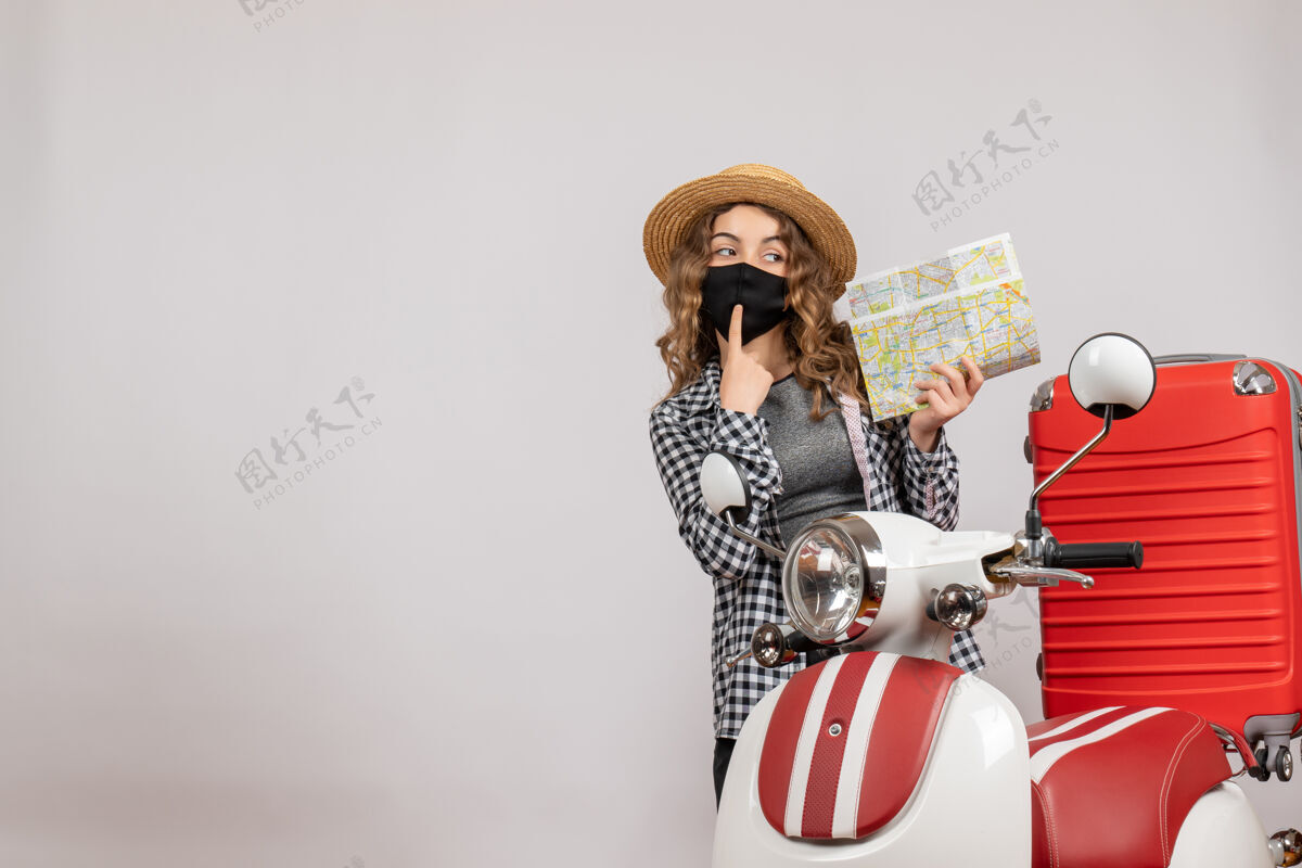 立场戴着黑色面具的酷酷少女手持地图站在红色轻便摩托车旁的正视图黄铜节日低音