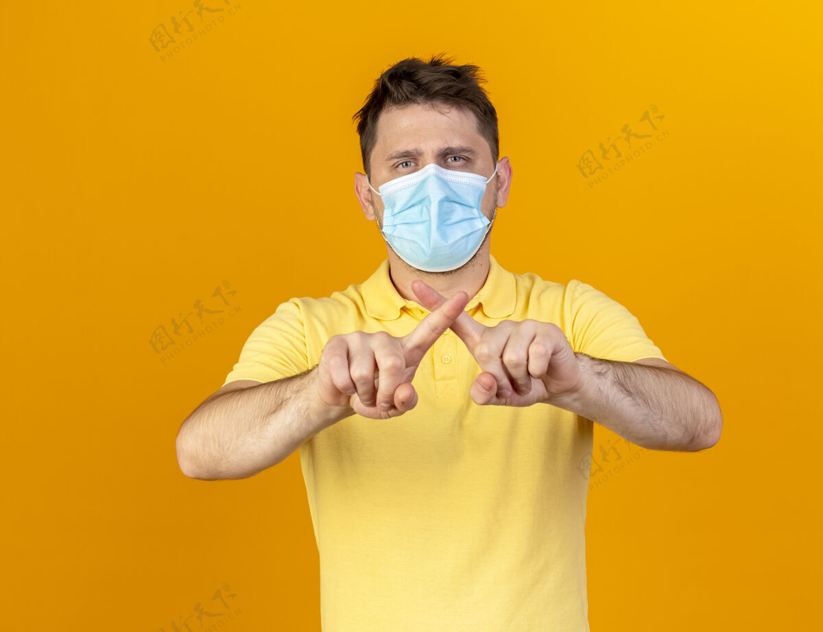 疾病自信的年轻金发病斯拉夫男子戴着医用口罩交叉手指示意没有迹象隔离在橙色墙上复制空间手势穿手指