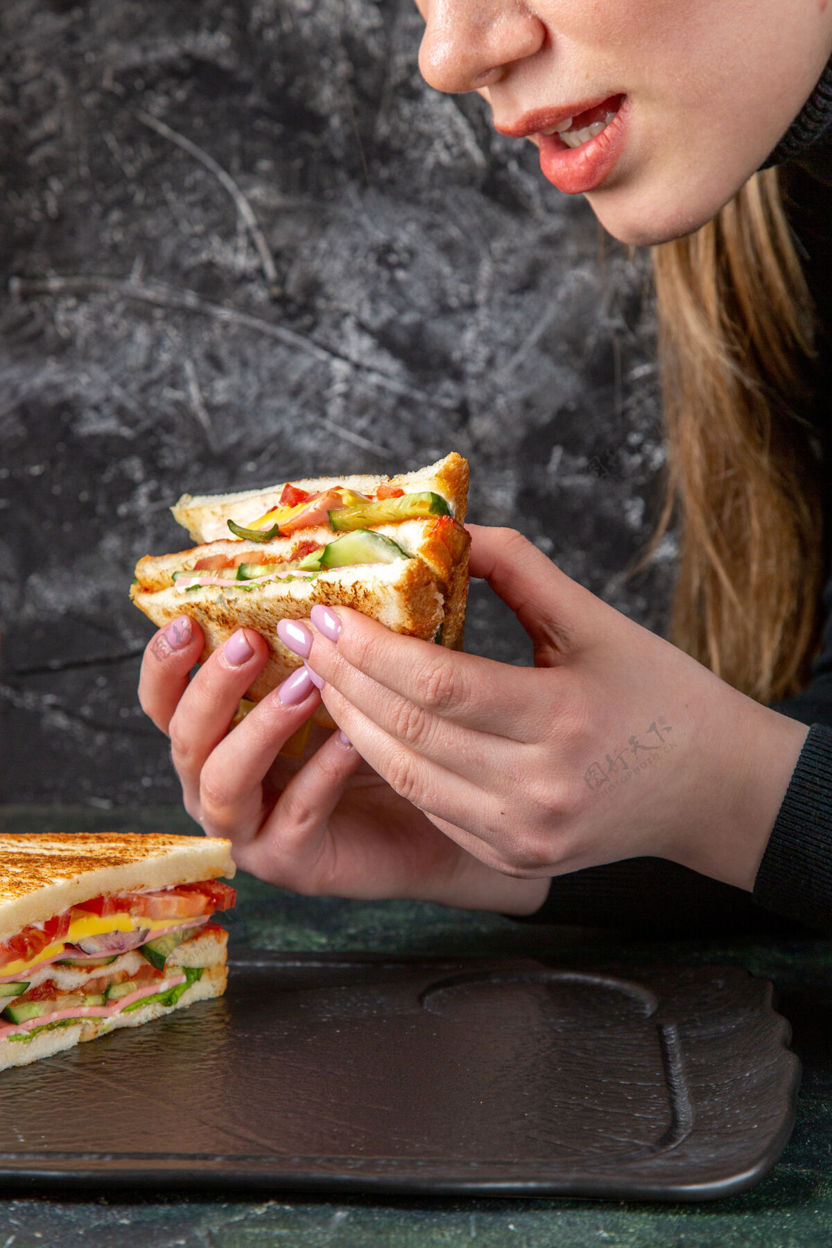 饮食正面图美味的火腿三明治正在黑暗的表面被女性吃掉前面黑暗三明治