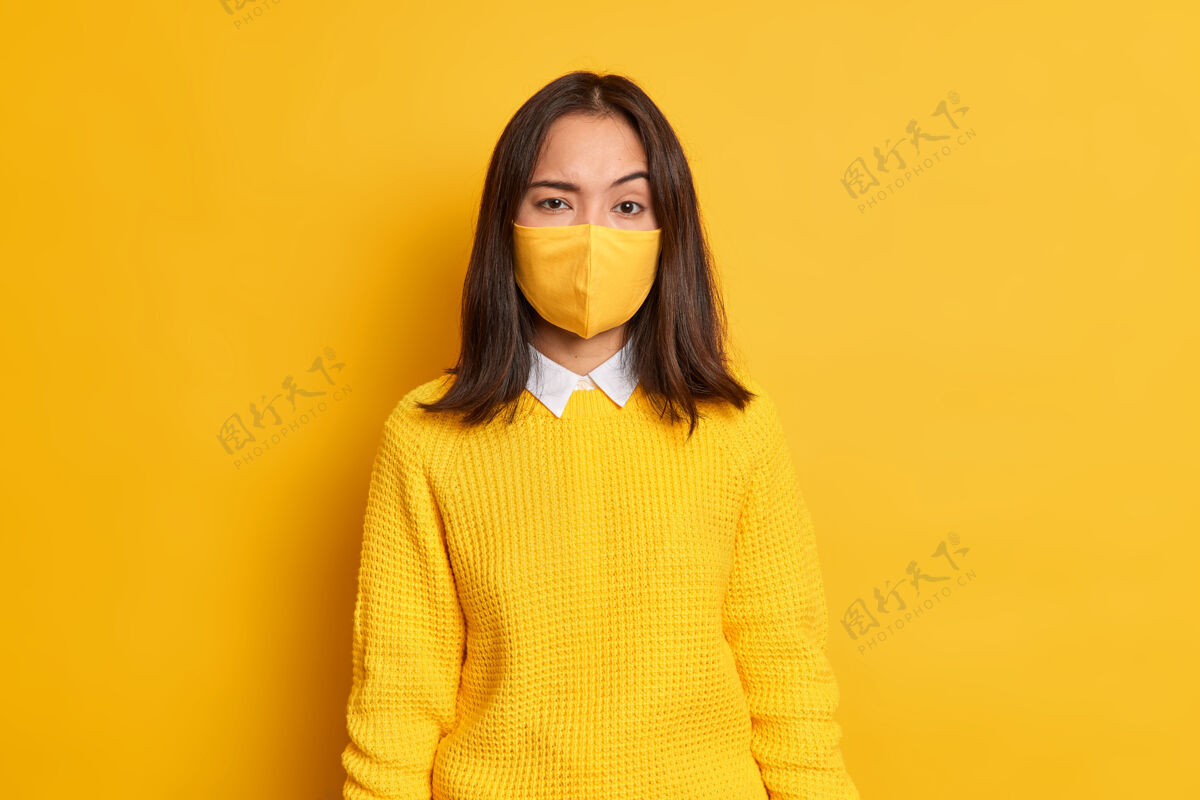流行一张严肃的亚洲年轻女子扬眉吐气的照片在冠状病毒大流行期间戴着一次性防护口罩呆在家里针织呆在家里穿着