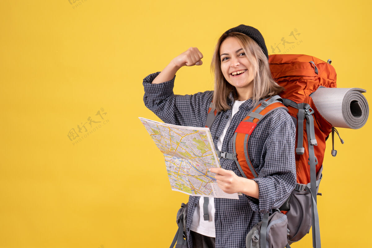 背包正面图是一位快乐的女旅行者 背着背包 地图上显示了她的手臂肌肉人时尚漂亮