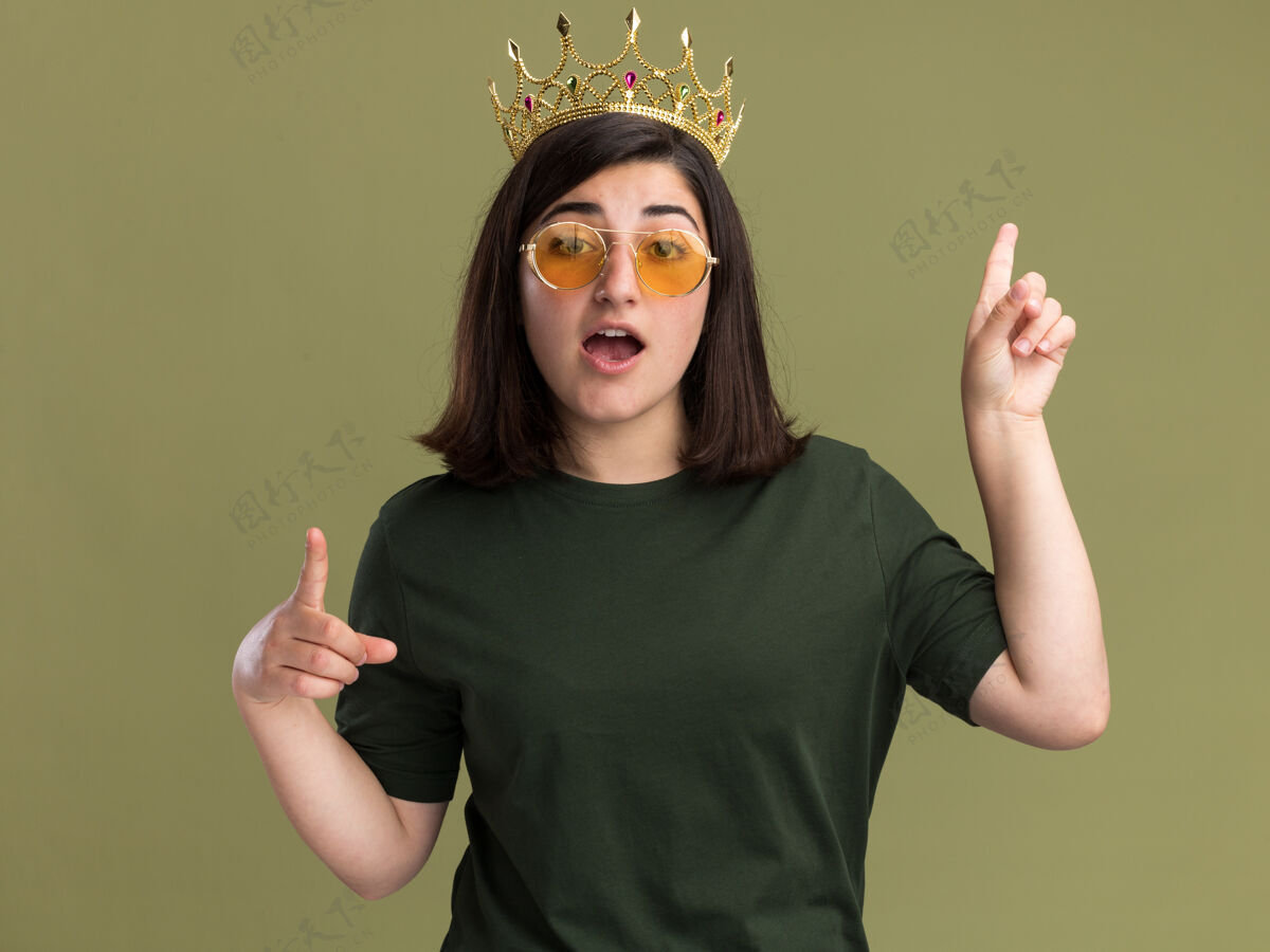 冠年轻漂亮的高加索女孩戴着太阳镜 头朝上 两只手放在橄榄绿上年轻尖手