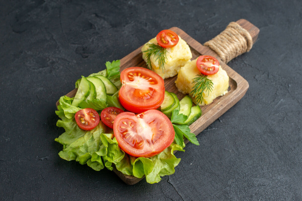 生菜侧视图切割新鲜番茄和黄瓜奶酪在木板上的黑色表面番茄晚餐黄瓜