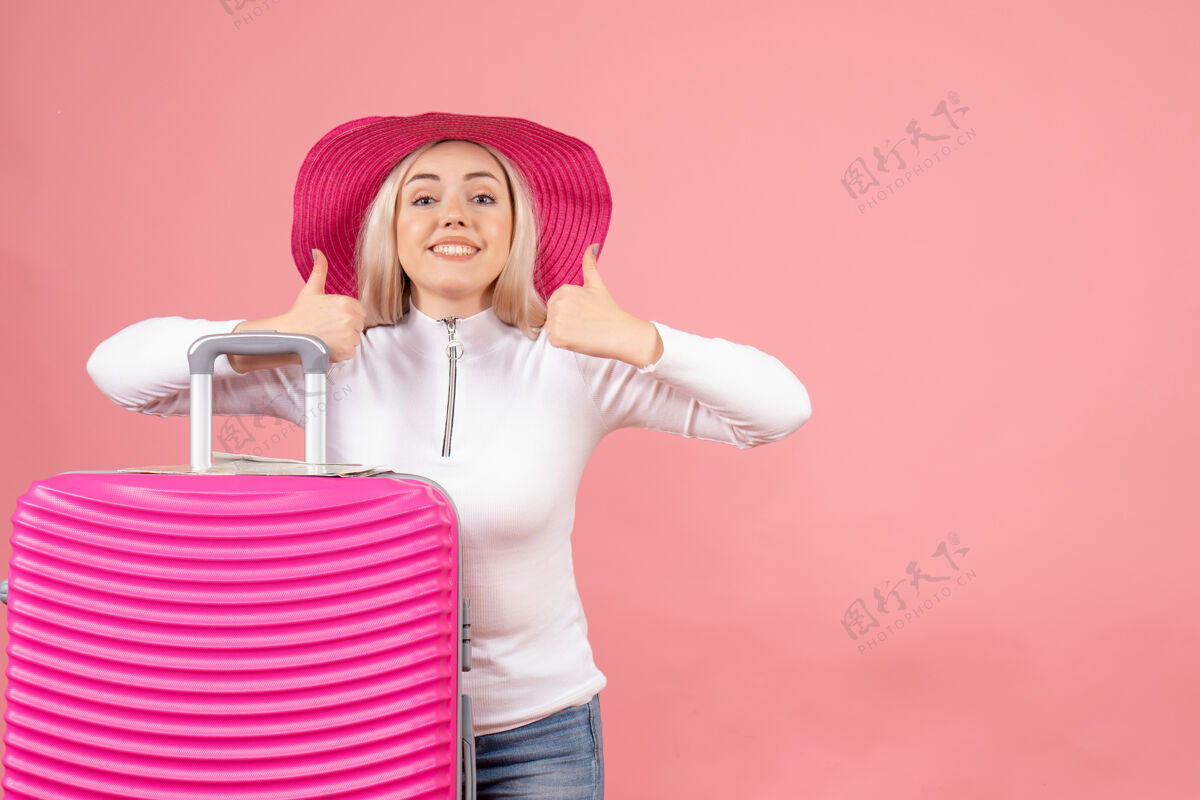 漂亮正面图快乐的金发女人拿着粉红色的手提箱竖起大拇指模型前面成人