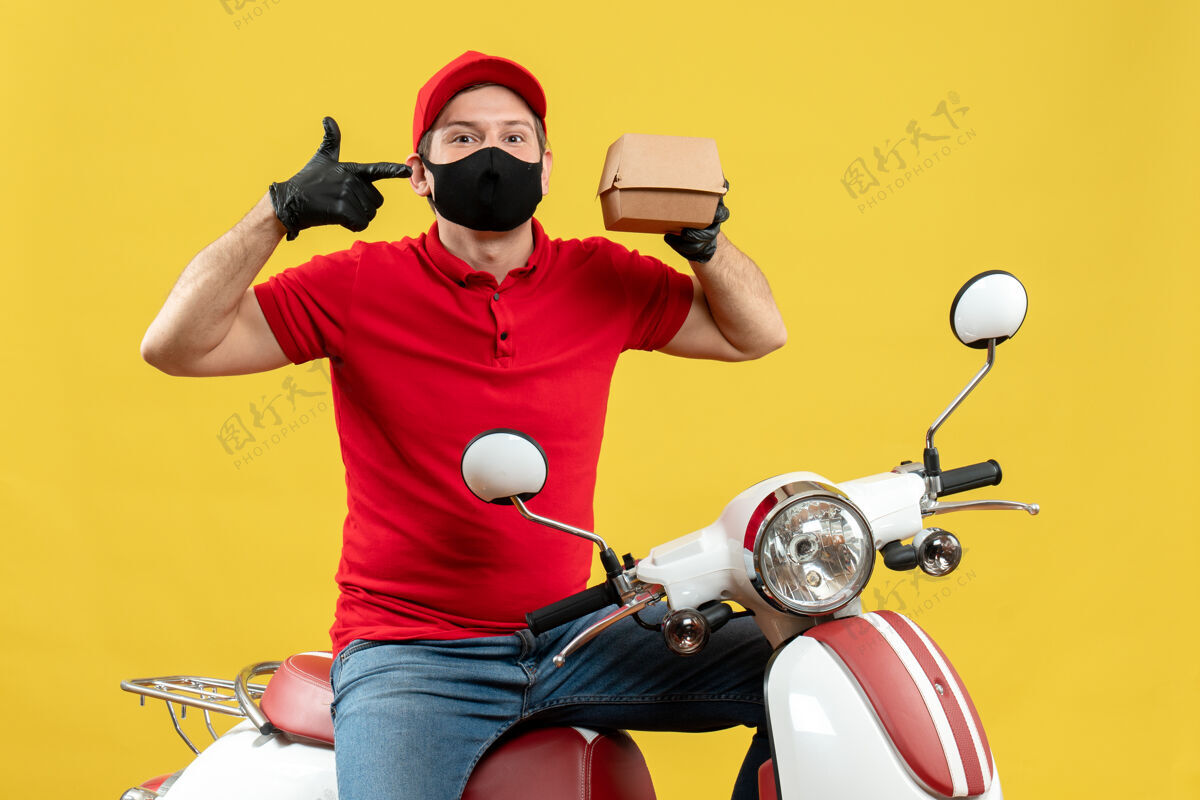 送货员俯视图微笑的送货员身穿红色上衣 戴着帽子手套 戴着医用面罩 坐在滑板车上 显示秩序衬衫手套摩托车