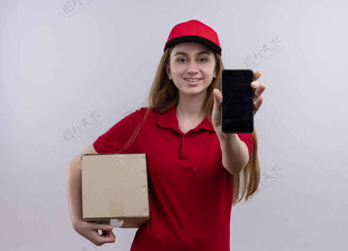 手机微笑着的年轻送货女孩 穿着红色制服 拿着盒子 在与世隔绝的白色空间里伸展着手机送货伸展年轻