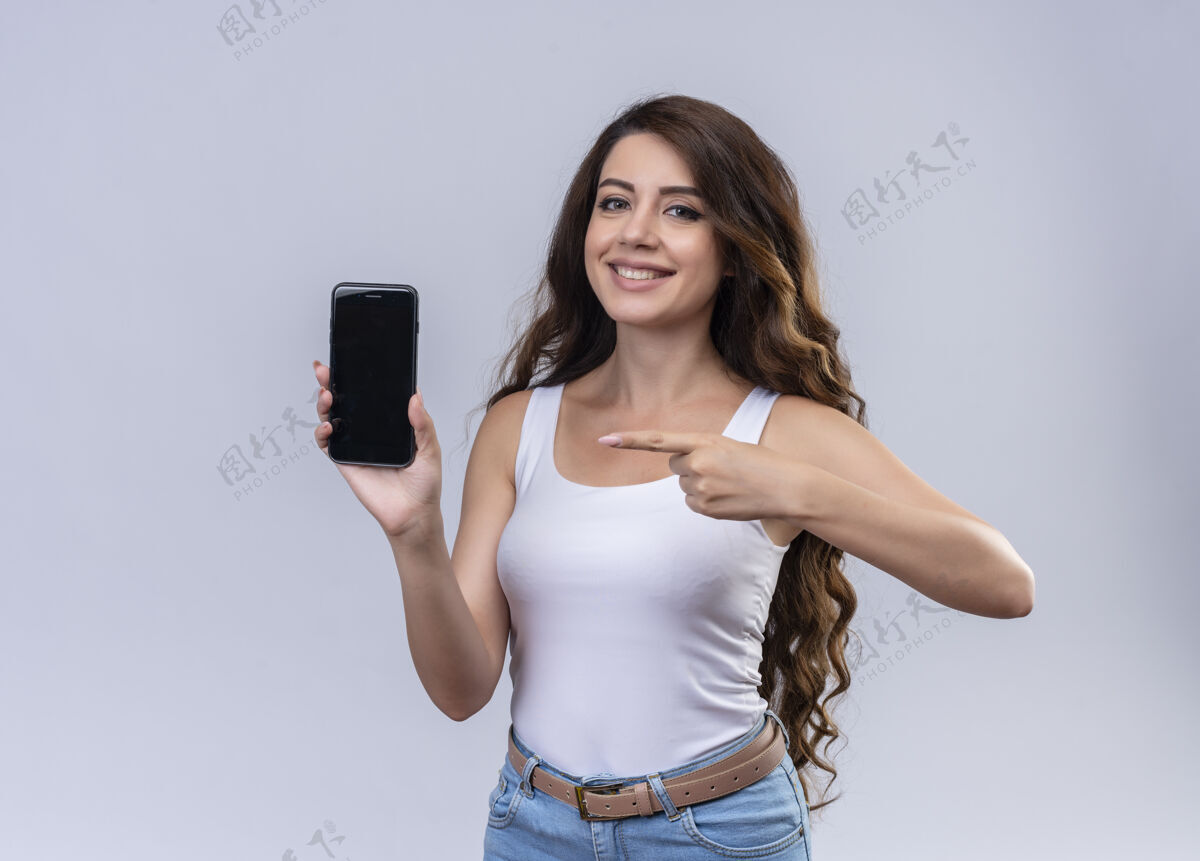 拿着微笑的年轻漂亮的女孩拿着手机 指着它与复制空间指向年轻电话
