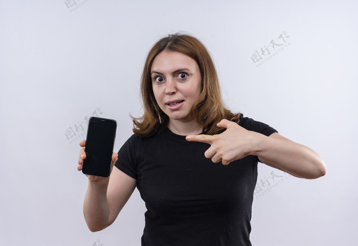 印象印象深刻的年轻休闲女子手持手机 指着它在孤立的白色空间女人指着年轻