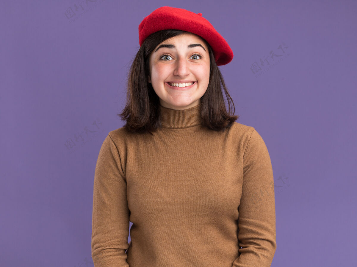 帽子兴奋的年轻漂亮的白人女孩戴着贝雷帽看着紫色的相机漂亮相机年轻