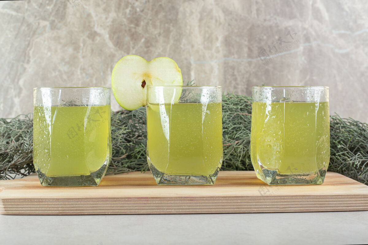 美味三杯果汁加苹果片放在木板上食品松枝新鲜