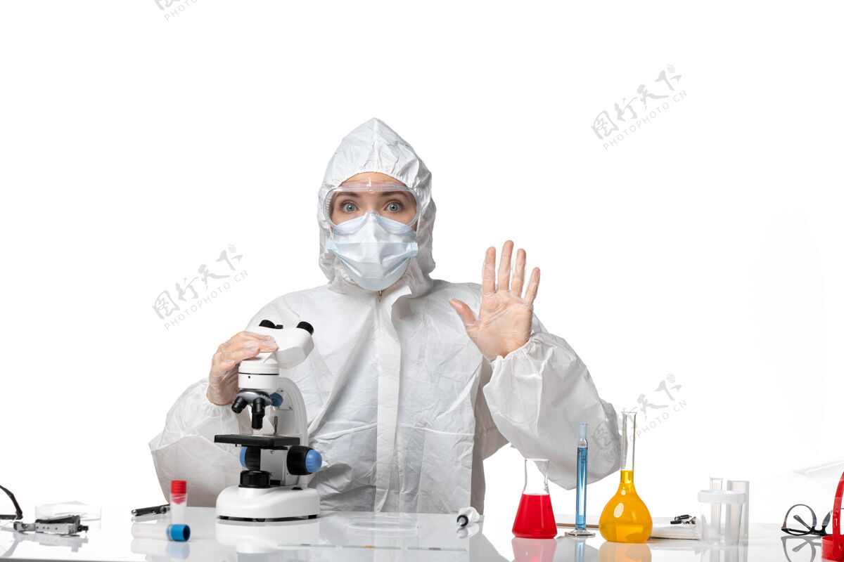 医疗正面图女医生穿着防护服 戴着口罩 在显微镜下观察白色背景病毒大流行时溅起的covid-防护病毒实验室外套